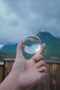 Cropped hand holding crystal ball against sky