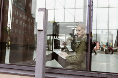 Thoughtful woman using laptop while looking through window at station