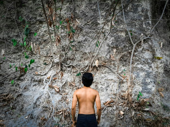 Rear view of shirtless man standing against rock