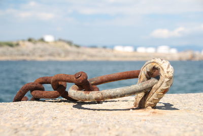 Close-up of rusty chain by sea against sky