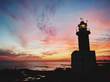 Lighthouse by sea against sky during sunset