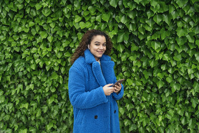 Young woman using phone while standing on green plant