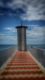 Lighthouse by pier against sky