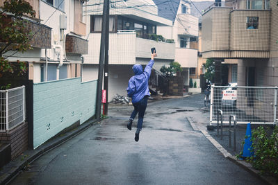 Rear view of boy jumping on street against buildings in city