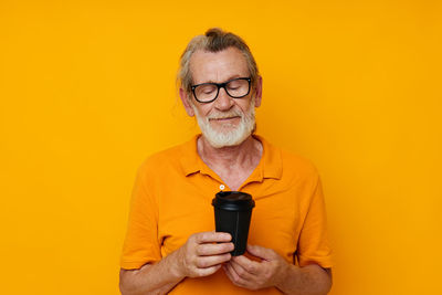 Portrait of young man holding trophy against yellow background