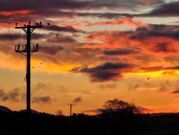 Low angle view of silhouette electricity pylon against sky during sunset