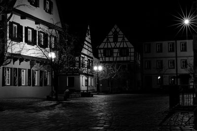 Illuminated street by buildings in city at night
