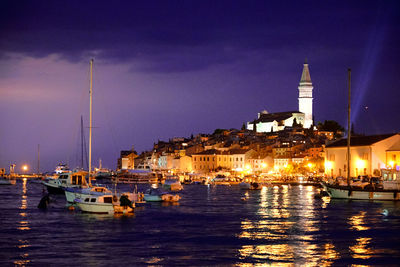 Sailboats moored in sea against sky at night