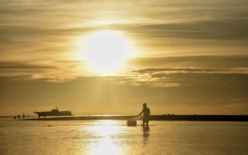 Silhouette man standing in sea against sky during sunset