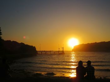 Silhouette people looking at sea against sky during sunset