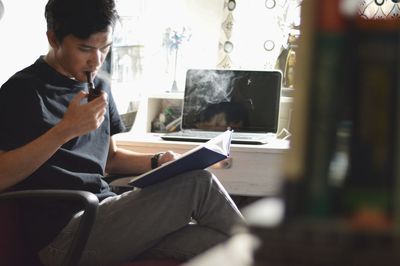 Man smoking pipe while reading book at home