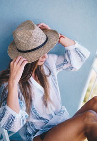 Woman wearing hat sitting on chair against wall