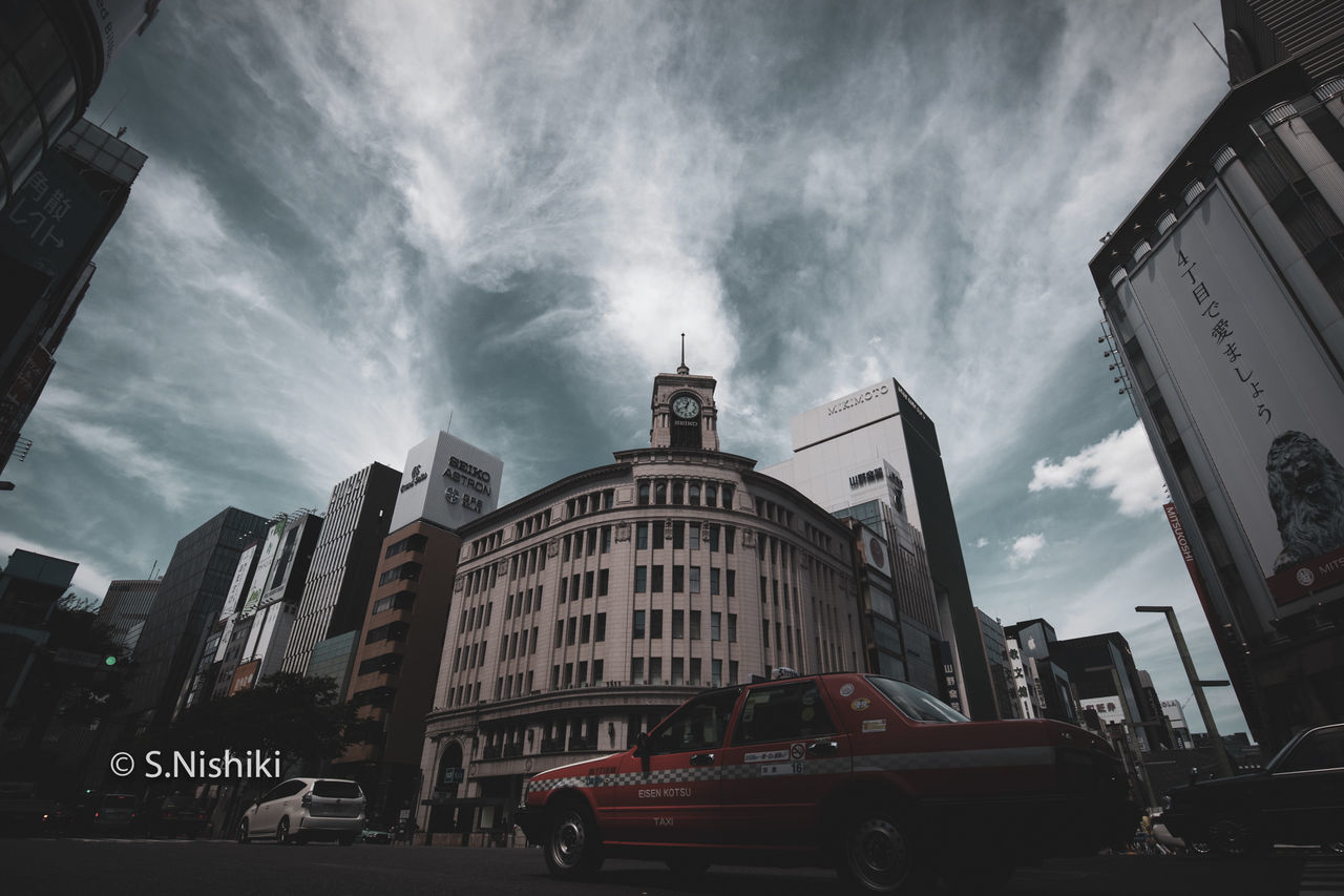 CARS ON ROAD AMIDST BUILDINGS AGAINST SKY