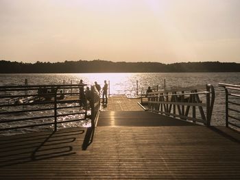 Silhouette people on pier over lake against sky during sunset