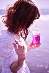 Side view of woman holding drink while standing against sea