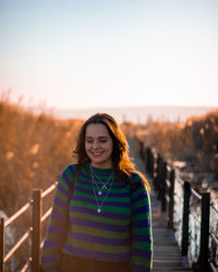 Portrait of woman standing on railing against sky