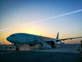 Airplane on runway against sky at sunset