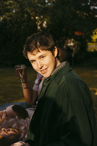 Side view portrait of smiling non-binary person with friends in back yard at sunny day