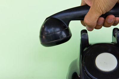 Close-up of hand holding telephone receiver against green background
