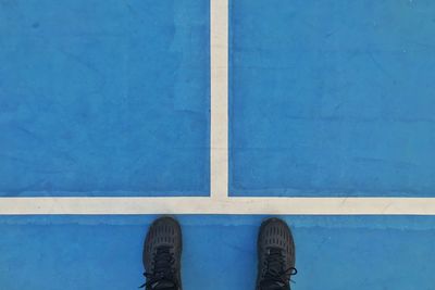 Low section of man standing on blue footpath