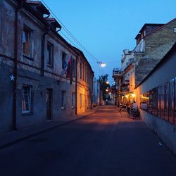 Illuminated street amidst buildings in city at dusk