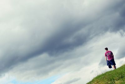 Rear view of man standing on field against cloudy sky