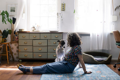 Side view of woman sitting on floor with dog at home