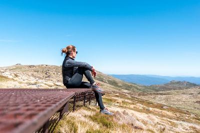 Man sitting on mountain against blue sky