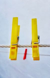 Close-up of yellow clothespins on clothesline against sky