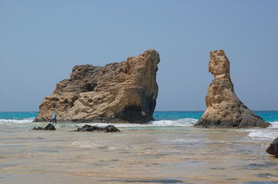 Rock formations at beach against clear blue sky