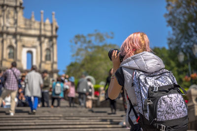 Woman photographing people while standing on staircase in city