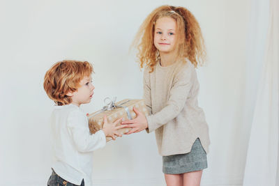 Portrait of girl giving gift to brother at home
