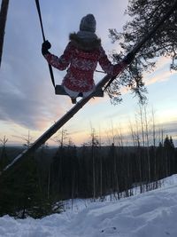 Woman standing on snow covered land against sky during sunset