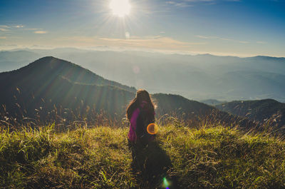 Woman standing on mountain against bright sun