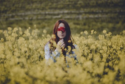 Portrait of beautiful woman with flower amidst oilseed rape field