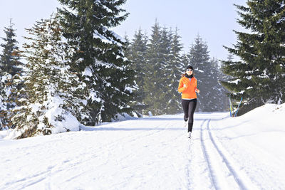 Woman running on snow covered field against sky