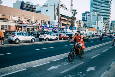 Man riding bicycle on road against buildings in city