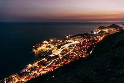 Aerial view of illuminated city by sea against sky at night