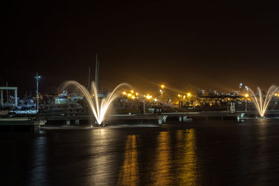 Illuminated harbor by river against sky at night