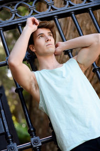 Low angle view of thoughtful young man standing against gate