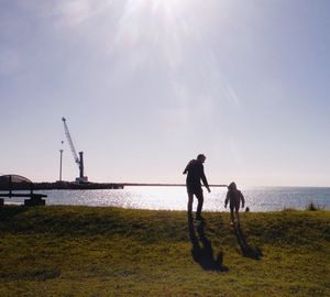 Father and son playing by sea against sky during sunny day