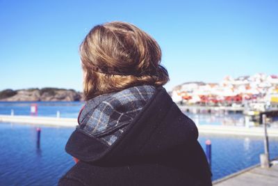 Rear view of woman standing by lake against clear blue sky