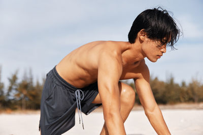 Portrait of shirtless young woman exercising at beach