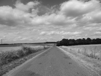 Empty road amidst field against sky