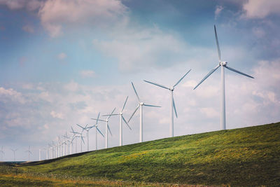 Wind turbines on hill against cloudy sky