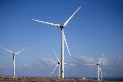 Windmills on field against clear blue sky