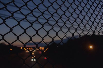 Close-up of chainlink fence against sky during sunset