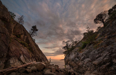 Rock formations at beach against sky during sunset