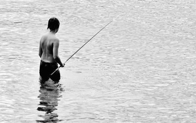 Rear view of shirtless man fishing in sea