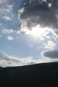 Low angle view of sun shining through clouds